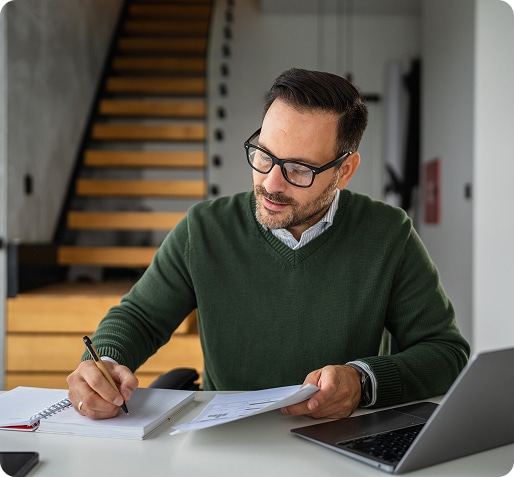 Man at desk with laptop working with notebook