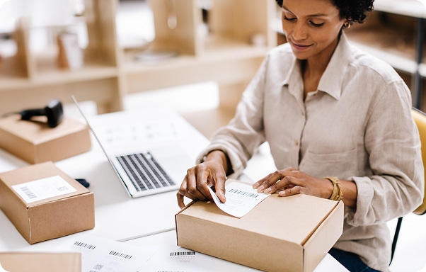 Woman at desk with laptop labeling boxes for shipping